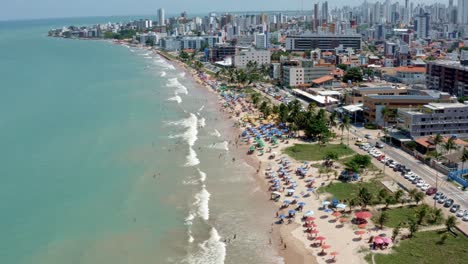 Rising-aerial-shot-of-intermares-beach-in-Cabedelo,-Brazil-with-Brazilians-and-tourists-enjoying-the-ocean-near-the-costal-capital-of-Joao-Pessoa-in-the-state-of-Paraiba-on-a-warm-sunny-summer-day