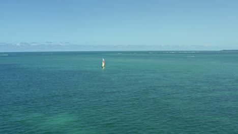 Dolly-in-aerial-shot-following-a-colorful-sail-boat-from-the-tropical-Bessa-beach-in-the-coastal-capital-city-of-Joao-Pessoa,-Paraiba,-Brazil-on-a-warm-sunny-summer-day