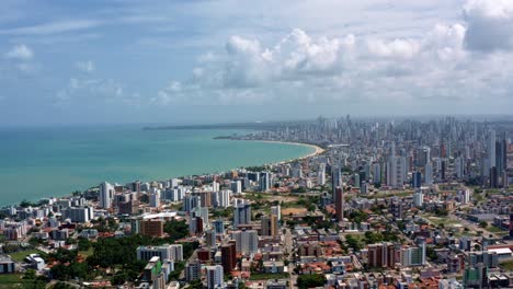 Rising-aerial-wide-shot-of-the-tropical-beach-city-of-Cabedelo,-Brazil-from-the-intermares-beach-near-Joao-Pessoa-with-skyscrapers-along-the-coastline-in-the-state-of-Paraiba-on-a-summer-day