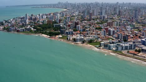 Tilt-up-aerial-wide-shot-of-the-tropical-capital-of-Joao-Pessoa-from-intermares-beach-in-Cabedelo,-Brazil-with-skyscrapers-along-the-coastline-in-the-state-of-Paraiba-on-a-warm-sunny-summer-day
