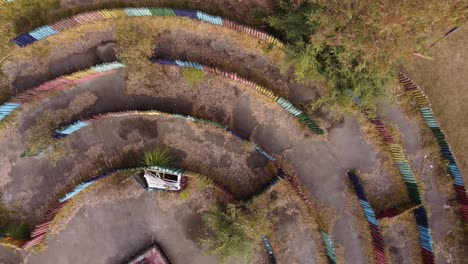 Aerial-view-of-old,-abandoned-and-vacant-outdoor-circular-labyrinth-made-of-colorful-wooden-logs