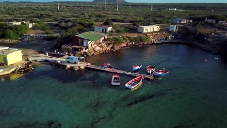 Aerial-orbit-of-a-small-dock-with-poor-houses-around,-fishing-bay,-Kanoa-Beach,-Curacao,-Dutch-Caribbean-island