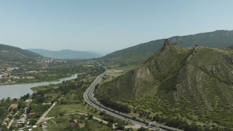 Aerial-View-Of-Vehicles-Driving-On-Road-By-The-Mountain-Along-Mtkvari-River-In-Mtskheta-Mtianeti,-Georgia