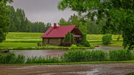 A-log-cabin-by-a-river-on-a-dreary,-rainy-day---time-lapse