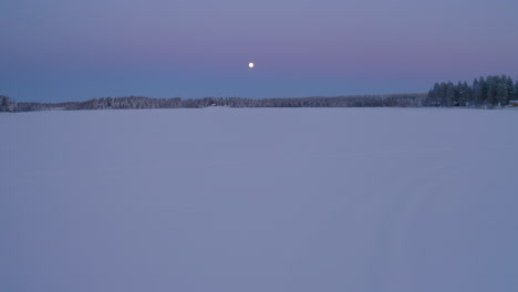 Aerial-view-moon-shining-above-vast-frozen-ethereal-Scandinavian-snow-covered-landscape