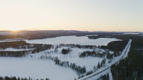Aerial-view-across-vast-Scandinavian-snow-covered-settlements-surrounded-by-Lapland-forest-landscape-under-sunrise-skyline