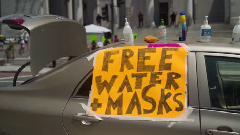 Ein-Schild-Mit-Der-Aufschrift-„Kostenloses-Wasser-Und-Masken“,-Das-Bei-Einer-Protestkundgebung-Vor-Dem-Rathaus-An-Ein-Auto-Geklebt-Wurde