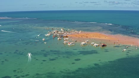 Trucking-right-aerial-shot-revealing-the-Red-Sand-Island-in-the-tropical-capital-Joao-Pessoa,-Paraiba,-Brazil-with-dozens-of-tourist-boats-docked-and-people-enjoying-the-ocean-on-a-warm-summer-day