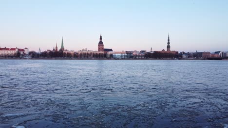 Icy-Daugava-river-and-towers-of-Riga-skyline,-low-altitude-aerial-view