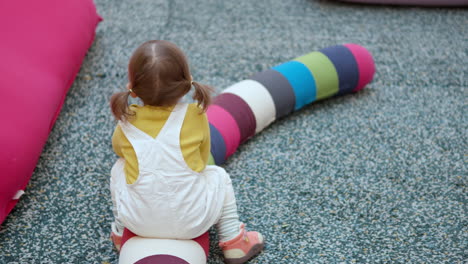 Funny-3-Year-Old-Little-Girl-Pretends-To-Ride-On-A-Colorful-Long-Pillow-In-A-Play-Area-Of-A-Shopping-Mall