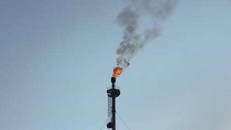 Black-smoky-fumes-billow-from-gas-burning-chimney-low-angle-close-up-against-blue-sky