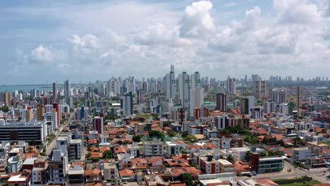 Truck-right-aerial-drone-shot-of-the-tropical-beach-town-of-Cabedelo-near-the-capital-city-of-Joao-Pessoa,-Paraiba,-Brazil-with-large-skyscrapers-and-rural-homes-below-on-a-warm-sunny-summer-day