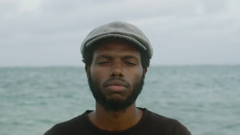 Shaky-close-up-of-a-young-black-African-man-looking-at-a-camera-with-a-serious-face-and-the-ocean-in-the-background