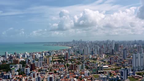 Descending-aerial-wide-shot-of-the-tropical-beach-city-of-Cabedelo,-Brazil-from-the-intermares-beach-near-Joao-Pessoa-with-skyscrapers-along-the-coastline-in-the-state-of-Paraiba-on-a-summer-day