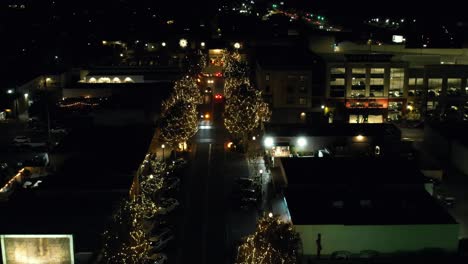 Small-town-during-Holiday-season-of-Christmas-times,-street-trees-lit-up-with-lights-as-cars-drive-down-street-at-night,-aerial-top-down-view