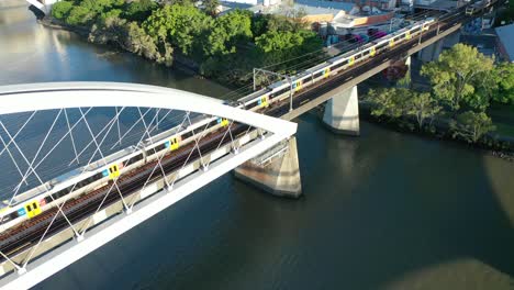 Trains-crossing-river-on-Brisbane's-iconic-Merivale-Railway-Bridge,-suspended-over-the-beautiful-Brisbane-River,-West-End,-South-Bank,-and-Brisbane-City-visible-in-this-stunning-drone-shot
