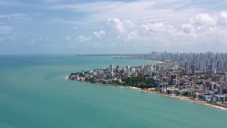 Dolly-in-aerial-wide-shot-of-the-tropical-capital-of-Joao-Pessoa-from-intermares-beach-in-Cabedelo,-Brazil-with-skyscrapers-along-the-coastline-in-the-state-of-Paraiba-on-a-warm-sunny-summer-day