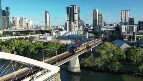 Two-trains-crossing-river-on-Brisbane's-iconic-Merivale-Railway-Bridge,-suspended-over-the-beautiful-Brisbane-River,-West-End,-South-Bank,-and-Brisbane-City-visible-in-this-stunning-drone-shot