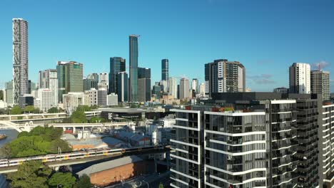 Aerial-drone-shot-of-Brisbane-cityscape-from-West-End,-camera-passes-close-to-an-apartment-building-with-rooftop-pool