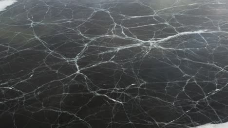 Dark-frozen-lake-in-Iceland-with-abstract-icy-veins-on-surface,-aerial