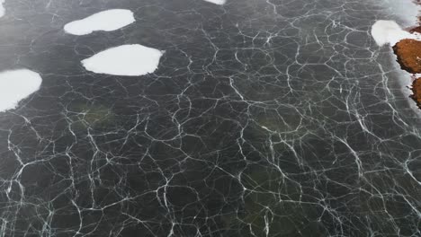 Frozen-lake-in-Iceland-with-white-cracked-lines-on-surface,-aerial