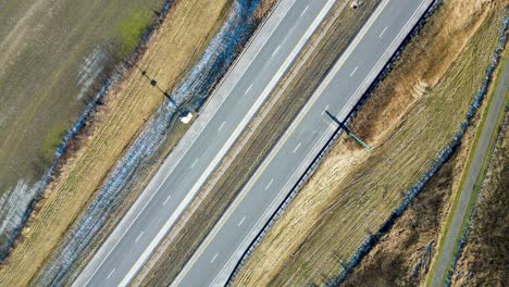 An-overhead-top-down-drone-shot-of-a-highway-in-the-winter-with-cars-passing-through-the-frame