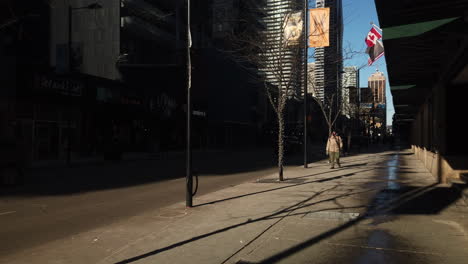Exterior-daytime-wide-shot-of-a-lone-figure-walking-southbound-down-a-sunny-Yonge-Street-in-Toronto