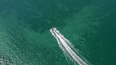 Rotating-aerial-drone-shot-following-a-jet-ski-on-beautiful-tropical-turquoise-ocean-water-at-the-Bessa-beach-in-the-coastal-capital-city-of-Joao-Pessoa,-Paraiba,-Brazil-on-a-warm-sunny-summer-day