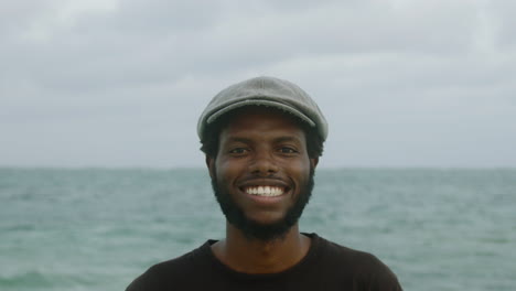 Close-up-of-a-handsome-beard-young-black-African-man-smiling-with-the-ocean-in-the-background