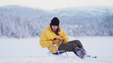 Hombre-Sentado-En-Un-Lago-Congelado-Para-Pescar---Pesca-En-Hielo-En-Indre-Fosen,-Noruega---Ancho