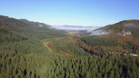 Aerial-rises-over-highway-through-forest-river-valley-in-Scotland
