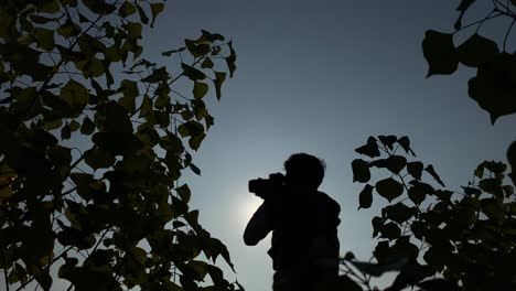 Silhouette-of-photographer-holding-camera,-points-and-shoot-at-sky-on-bright-day