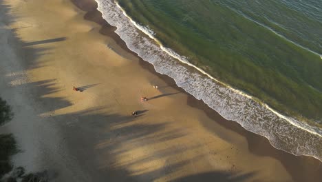Aerial-orbit-shot-of-family-having-fun-on-sandy-beach-during-golden-hour-with-Ocean-Waves