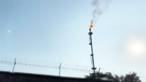 Fire-burning-emitting-Co2-in-air,-gas-flare,-industrial-area,-static,-behind-fence