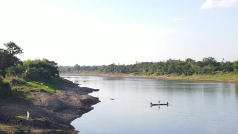 Toma-Aérea-Cinematográfica-De-Un-Pequeño-Bote-De-Madera-Con-Pescadores-Capturando-Peces-Usando-Una-Red-Al-Estilo-Tradicional-En-El-Río-Surma,-Bangladesh