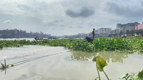 Fisherman-on-small-boat-in-Buriganga-river,-surrounded-by-water-hyacinth-in-Dhaka,-Bangladesh