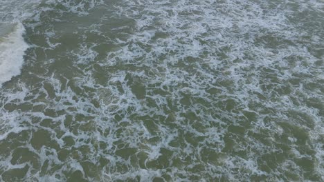 Aerial-birdseye-view-of-big-stormy-waves-breaking-against-the-white-sand-beach,-overcast-day,-seashore-dunes-damaged-by-waves,-coastal-erosion,-climate-changes,-wide-drone-shot-moving-forward