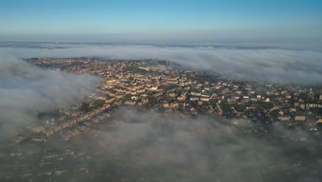 Cinematic-aerial-drone-point-of-view-UK-cityscape-during-sunrise,-early-morning-landscape,-residential-building-rooftops-at-dense-fog,-misty-weather