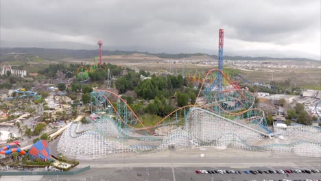 Six-flags-Magic-Mountain-theme-park-in-Valencia,-California,-roller-coaster-rides,-aerial-pullback-on-cloudy-day