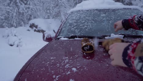 Person-Shakes-Off-Snow-From-Gloves-And-Beanie-Hat-On-The-Car-Hood-In-Winter
