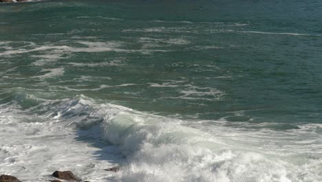 Clear-green-ocean-surf-wave-breaks-in-white-foam-onto-rocky-beach