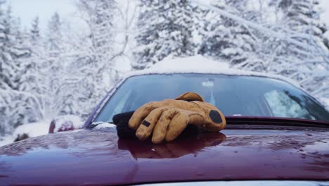 Strickmütze-Und-Handschuhe,-Die-Im-Winter-Auf-Die-Motorhaube-Des-Autos-Geworfen-Werden,-Während-Das-Dach-Schneebedeckt-Ist