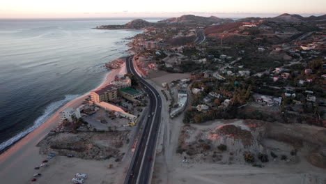 Drone-view-flying-over-road-along-coast-of-los-cabos,-Mexico-with-beaches-and-ocean