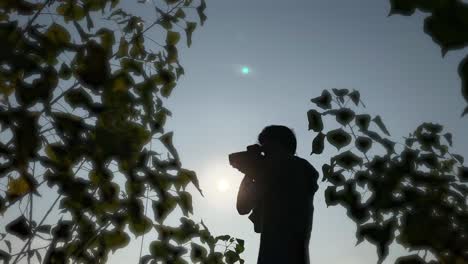 Silhouette-of-photograher-holding-DSLR-camera,-shooting-in-nature,-bright-sky