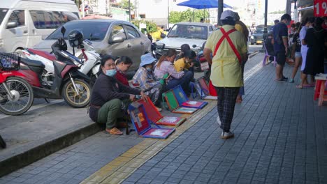 Shot-of-a-group-of-ladies-sitting-on-the-pavement-selling-lottery-tickets-along-the-roadside-in-Songkhla-Province,-Thailand-at-daytime