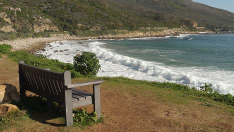 Bench-overlooks-surf-waves-breaking-onto-small-rocky-beach-in-Cape-town