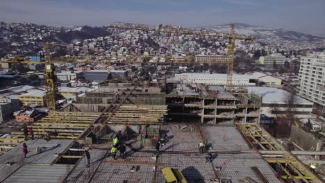Flying-over-construction-site-with-workers-and-crane-moving-construction-materials-in-the-winter