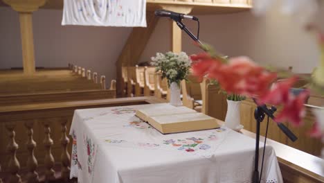 Aufgeschlagene-Bibel-Auf-Kleinem-Tisch-In-Der-Kirche,-Die-Hinter-Blumen-Zum-Vorschein-Kommt