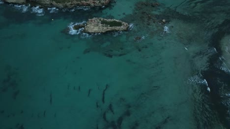 Cinematic-drone-reveal-of-small-island-rock-with-waves-lapping-up-against-the-shoreline-in-Spain