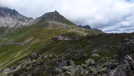 Aerial-flyover-rocky-and-mossy-mountains-of-Switzerland-with-hut-in-background-during-cloudy-day